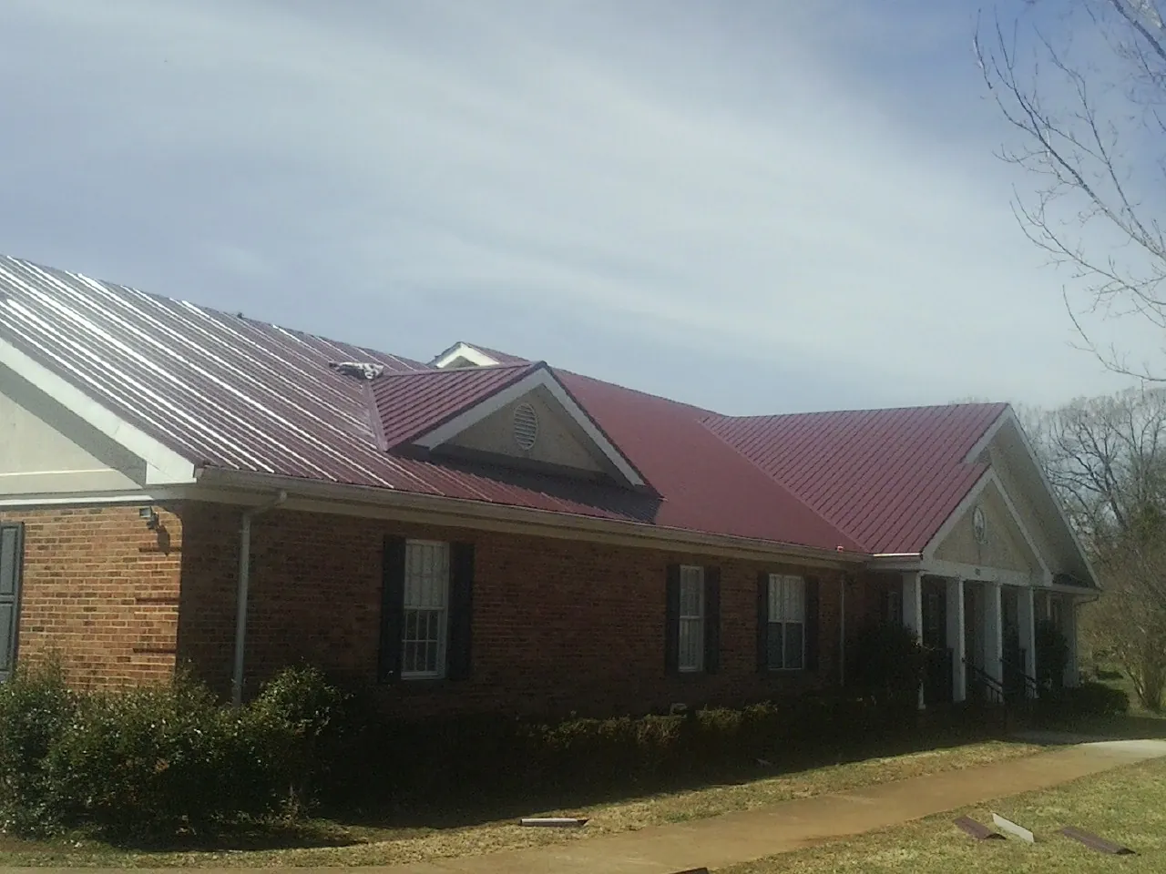 Red metal roof with gabled entries on a long brick building, from a Hail Damage Roof Repair job in South Woodstock
