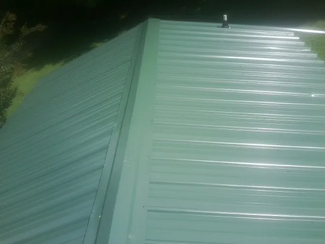 New green metal panels meeting at the ridge of a roof — Flat Roof Repair work by our crew in South Woodstock