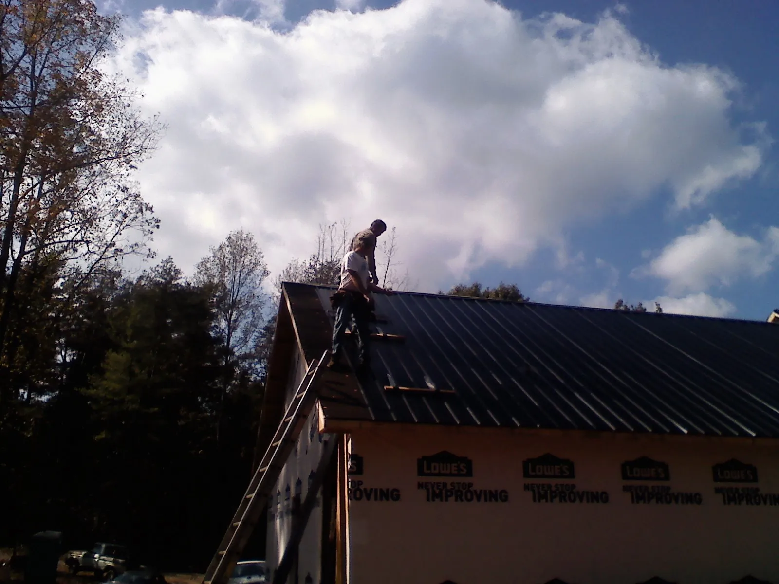 Roofer fastening dark metal panels high against a cloudy sky, from a Roof Inspection job in South Woodstock