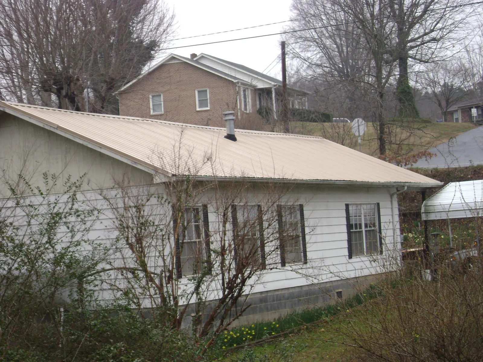 Tan metal roof on a white sided house set into a hillside — Commercial Roofing by Roofing Brothers in South Woodstock